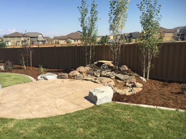 Artificial turf installation with boulders and xeric plants in Colorado backyard.
